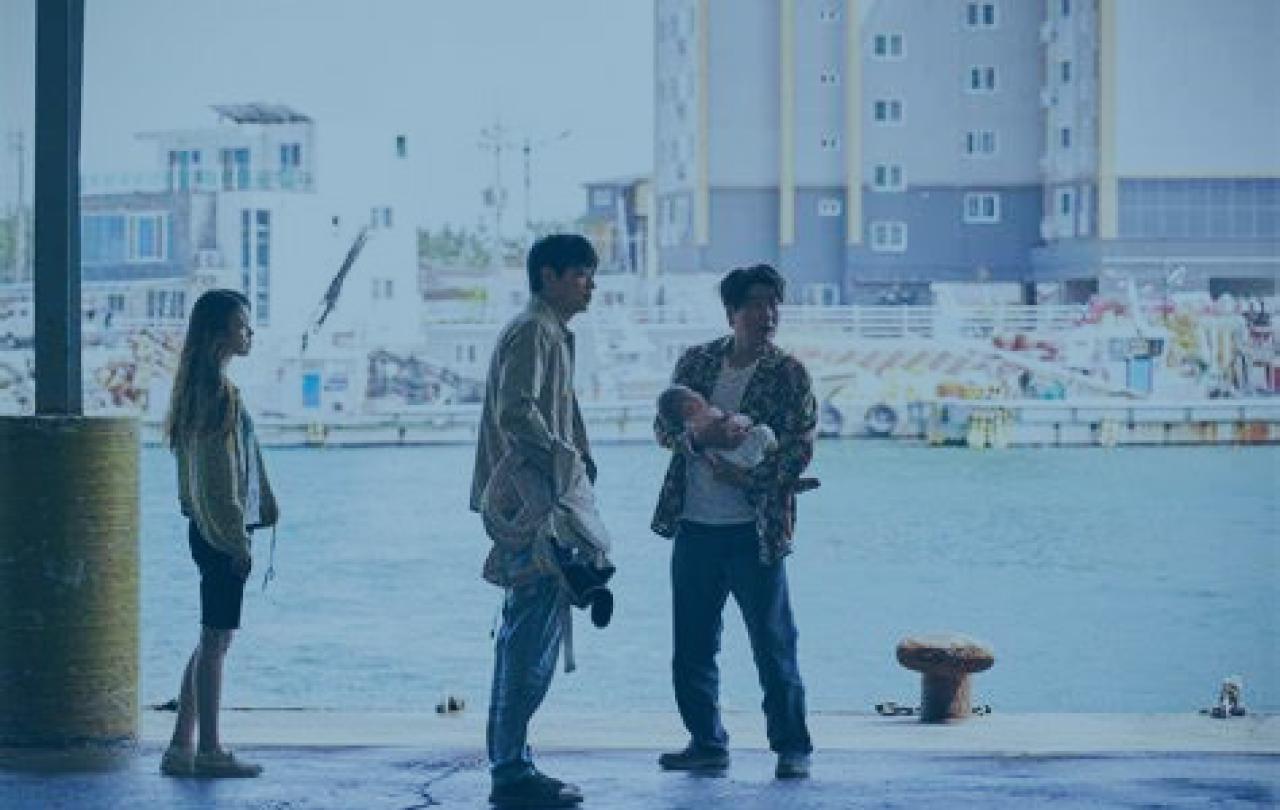 Three people, one carrying a baby, stand on a dock side at a harbour