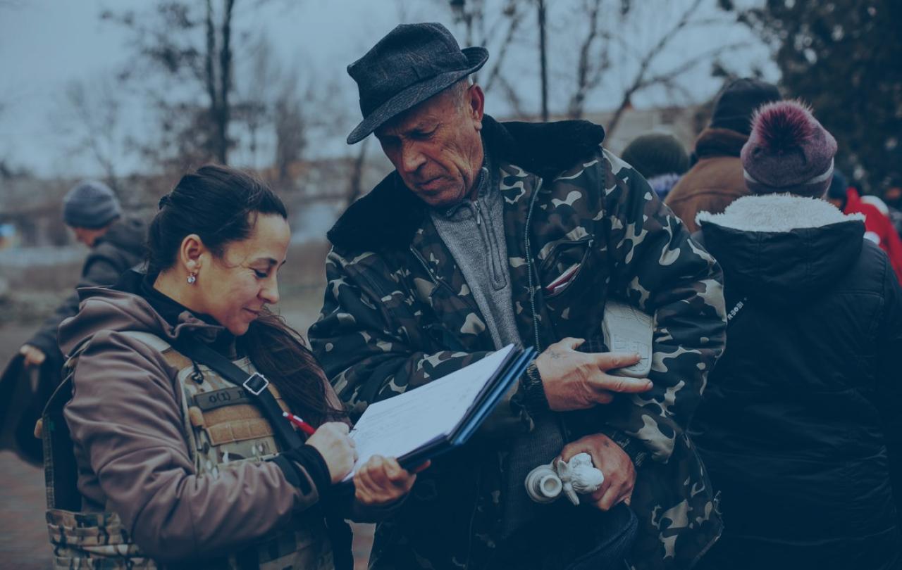 An aid worker and a local resident consult a list as they stand outside in a battle-affected town.