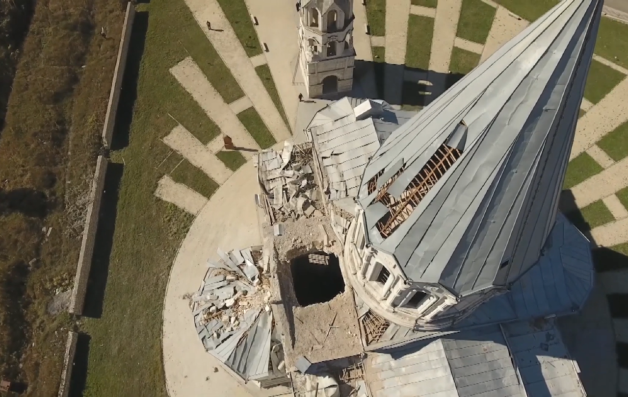 An aerial view looking down the damaged spire of a cathederal to a holes in the roof caused by shelling.