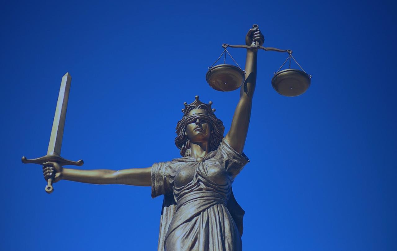 A statue of Justice holds a sword aloft in one hand, and set of scales in the other.