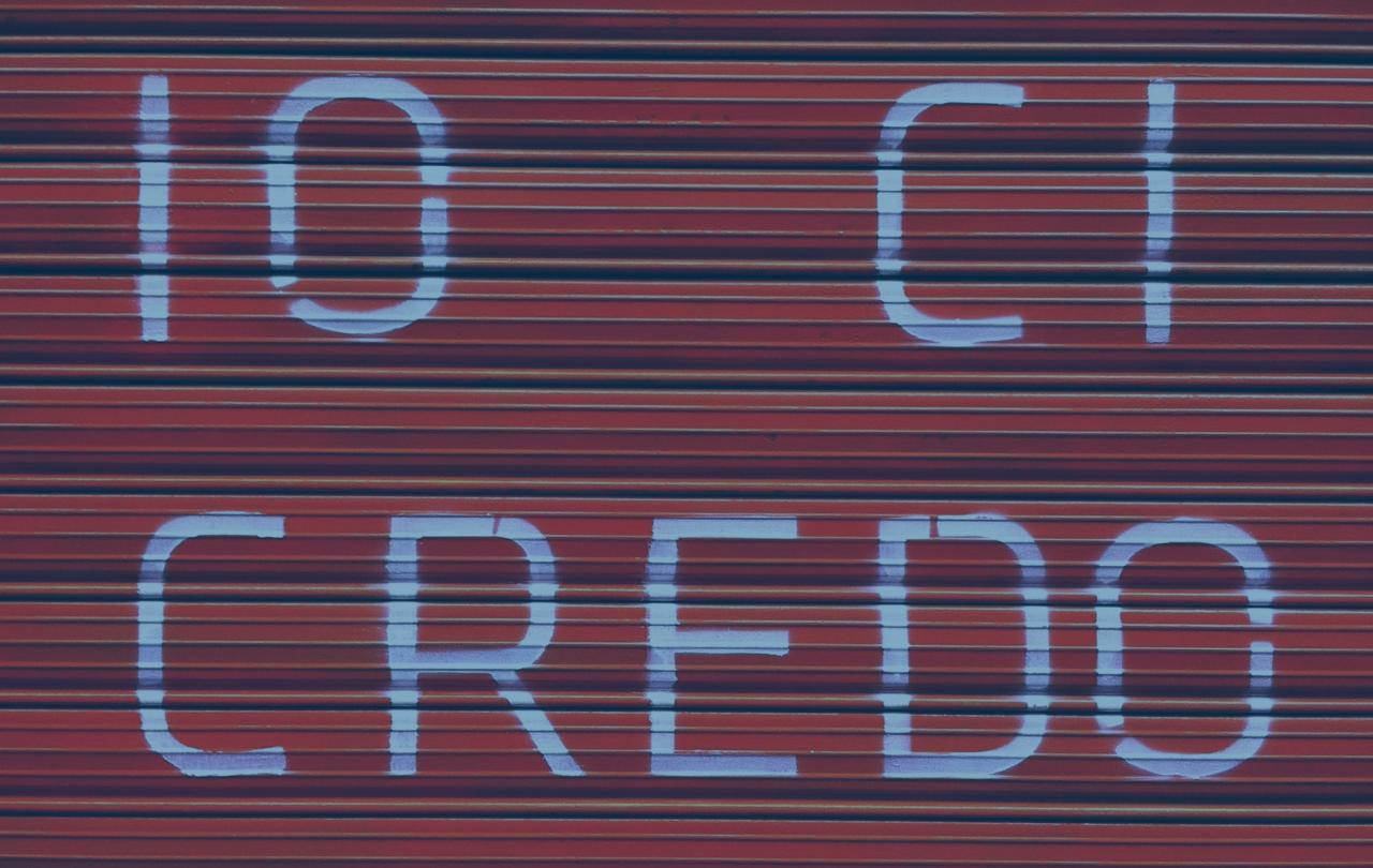 A red shutter door bears a large painted message reading 'io ci credo'