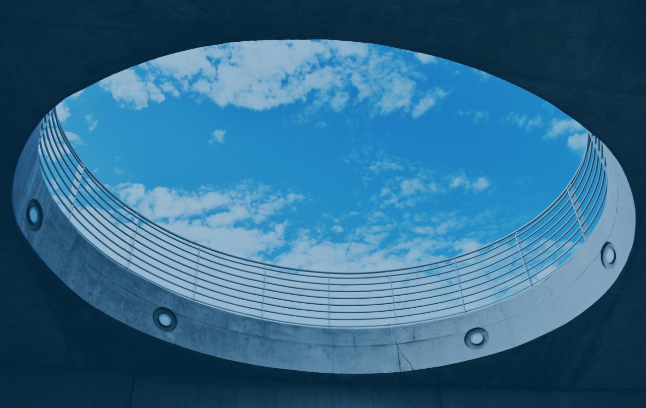 A cloud-dappled s blue sky is viewed through a large circular opening, from below.  