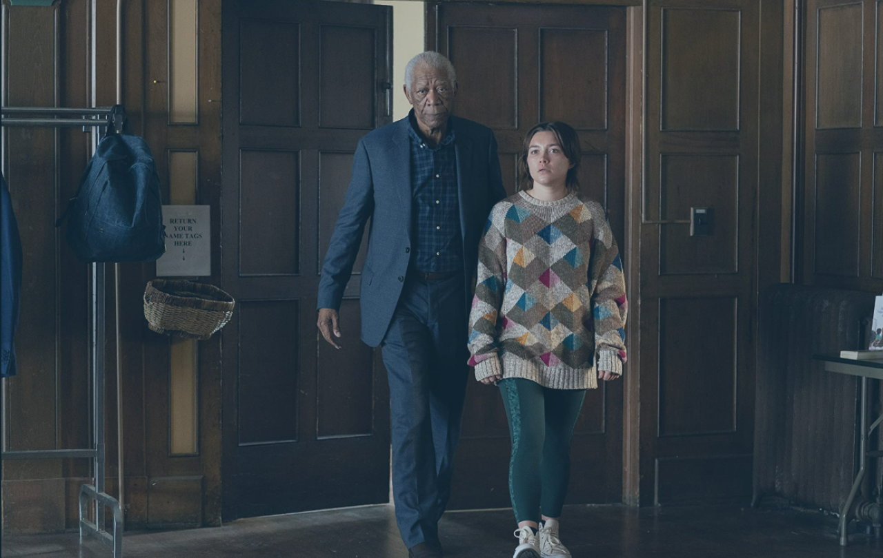 An old man accompanies a young woman into a wood-panelled hall, both look aprehensive.