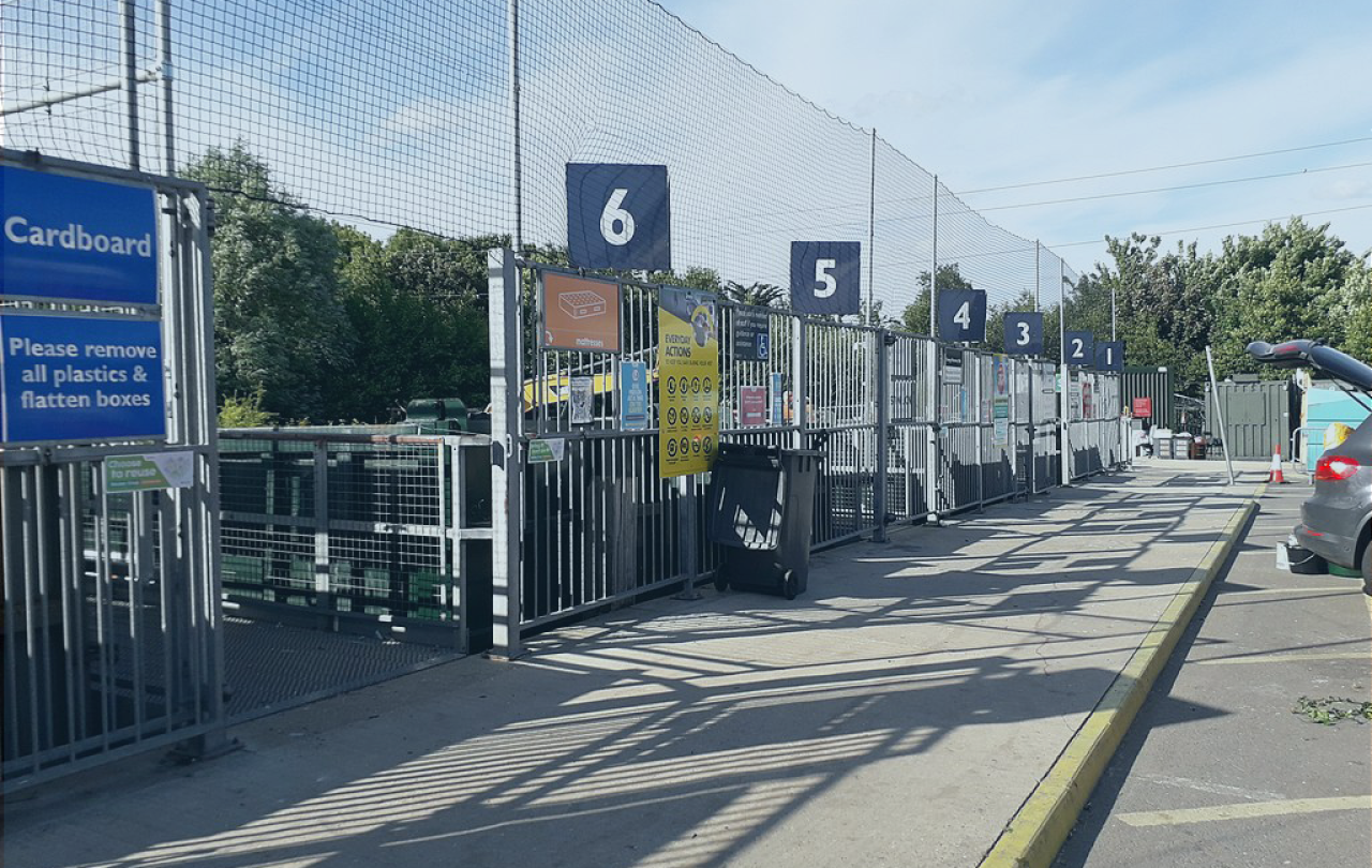 A recyling centre with numbered bays and high netting to catch wind-blown waste.