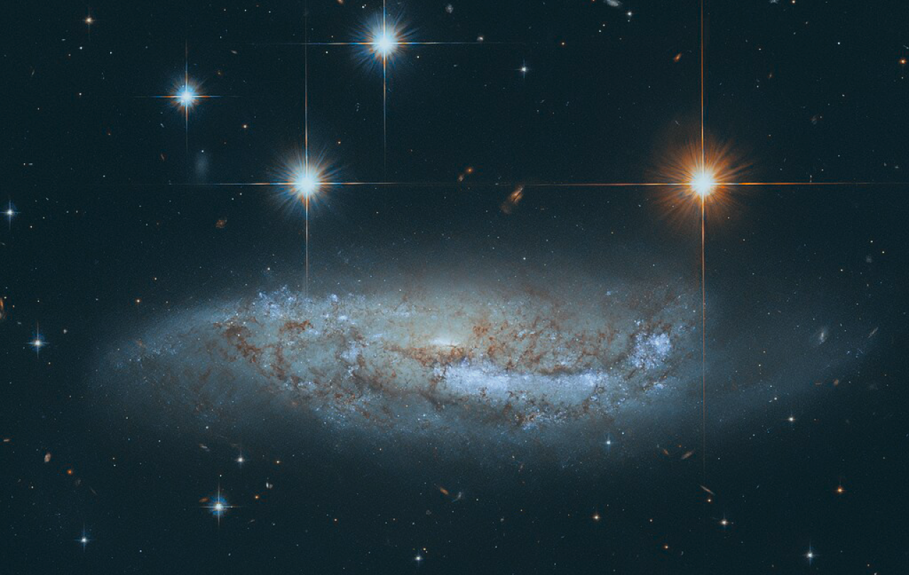 Four stars scintilate above a spiral galaxy viewed from the side.
