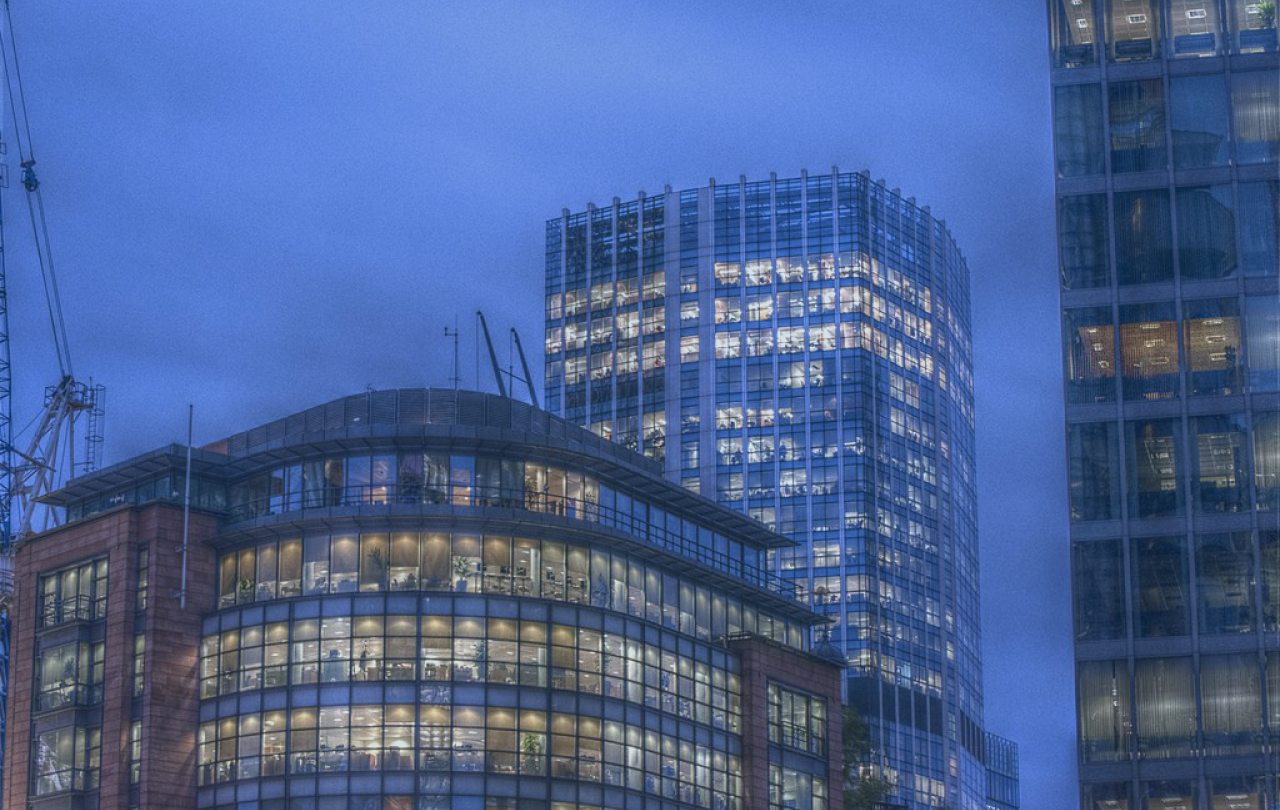 At twlight, the lit office windows of two tower blocks contrast with a darkening sky