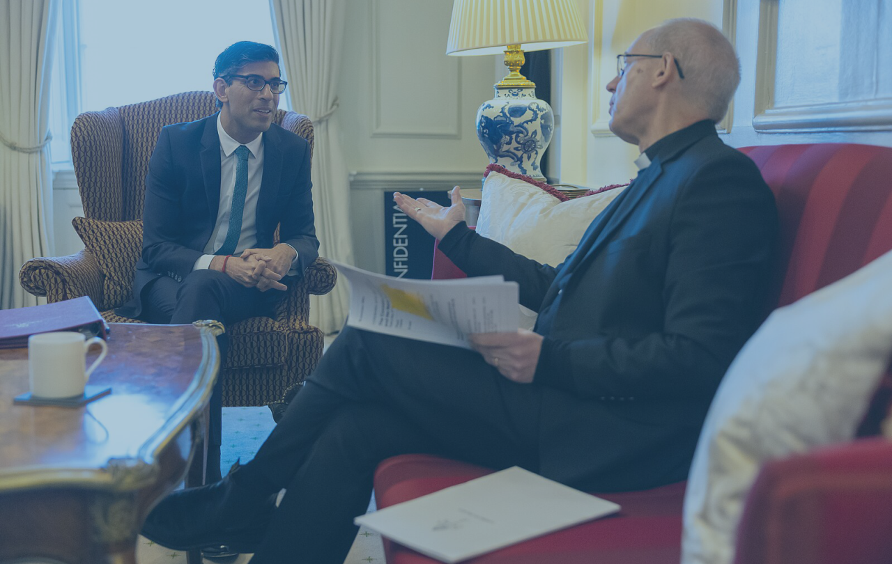 Prime minister Rishi Sunak leans forward out a lounge chair while the Archbishop of Canterbury talks and gestures while sitting on a sofa.