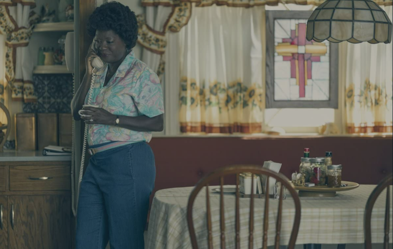 A woman stands in a kitchen diner hold a phone with a cord.