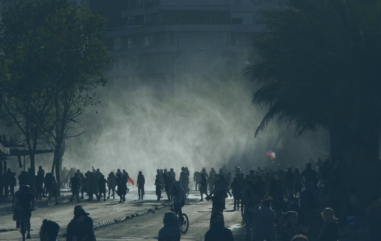 A loose rabble of a protest in the street is siluhetted against light and a shower of rain