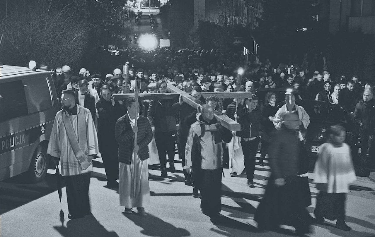 A Good Friday procession of people and priests hold a cross horizontal above their heads.