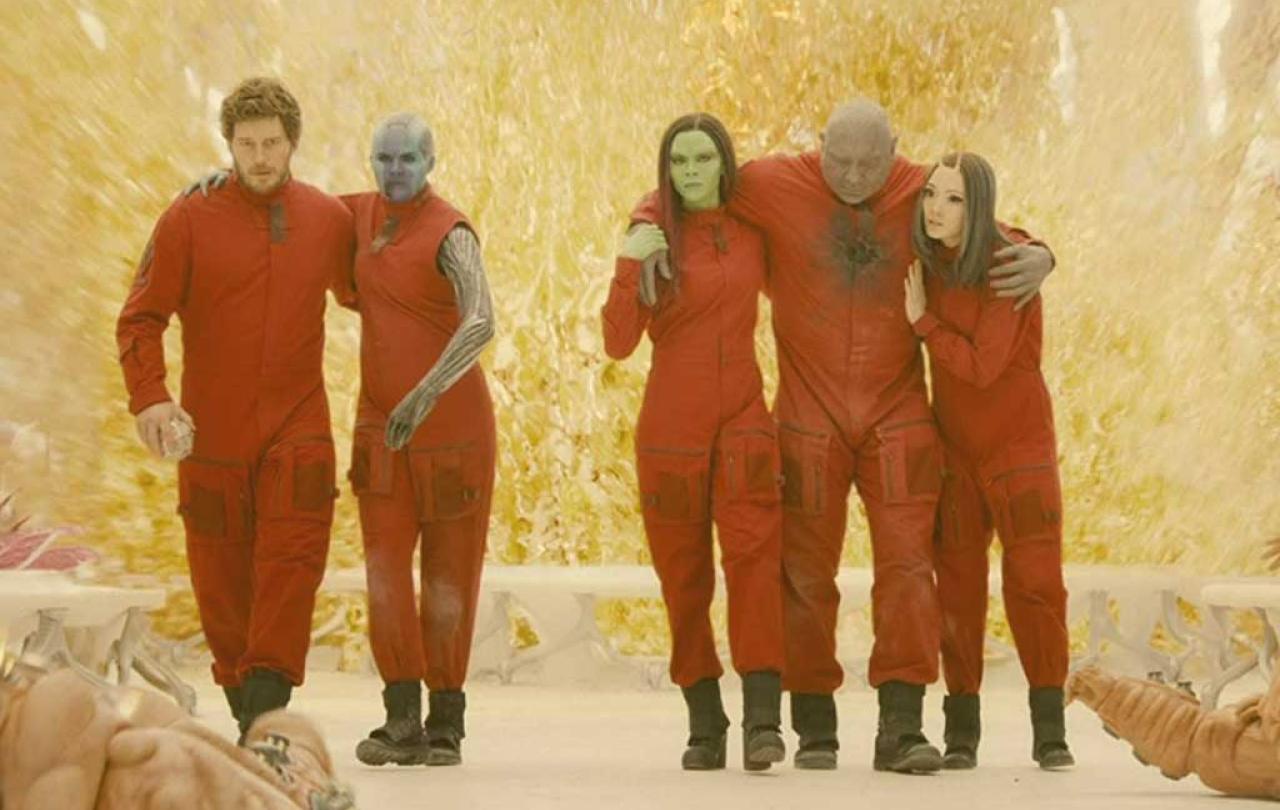 Five people in red jump suits help each other stand together.