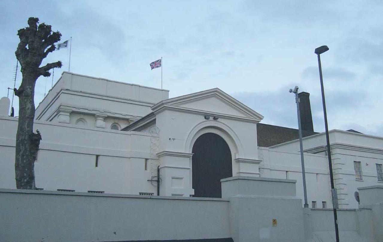 An arched gateway to a prison sits behind a low raised wall. No windows are visible