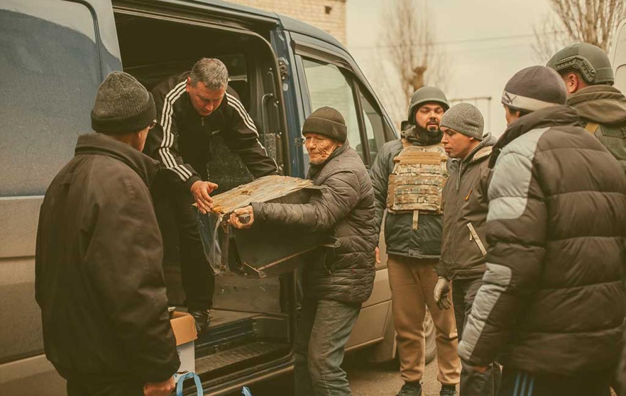 People help unload aid parcels from the side of a van, some wearing body armour.