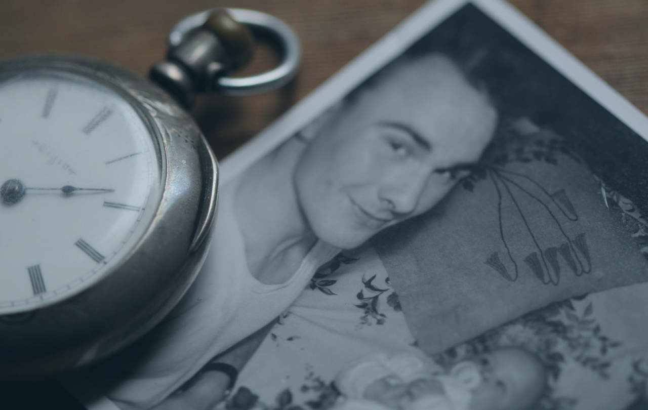 A pocket watch rests next to a black and white photograph of a father lying beside a new born baby.