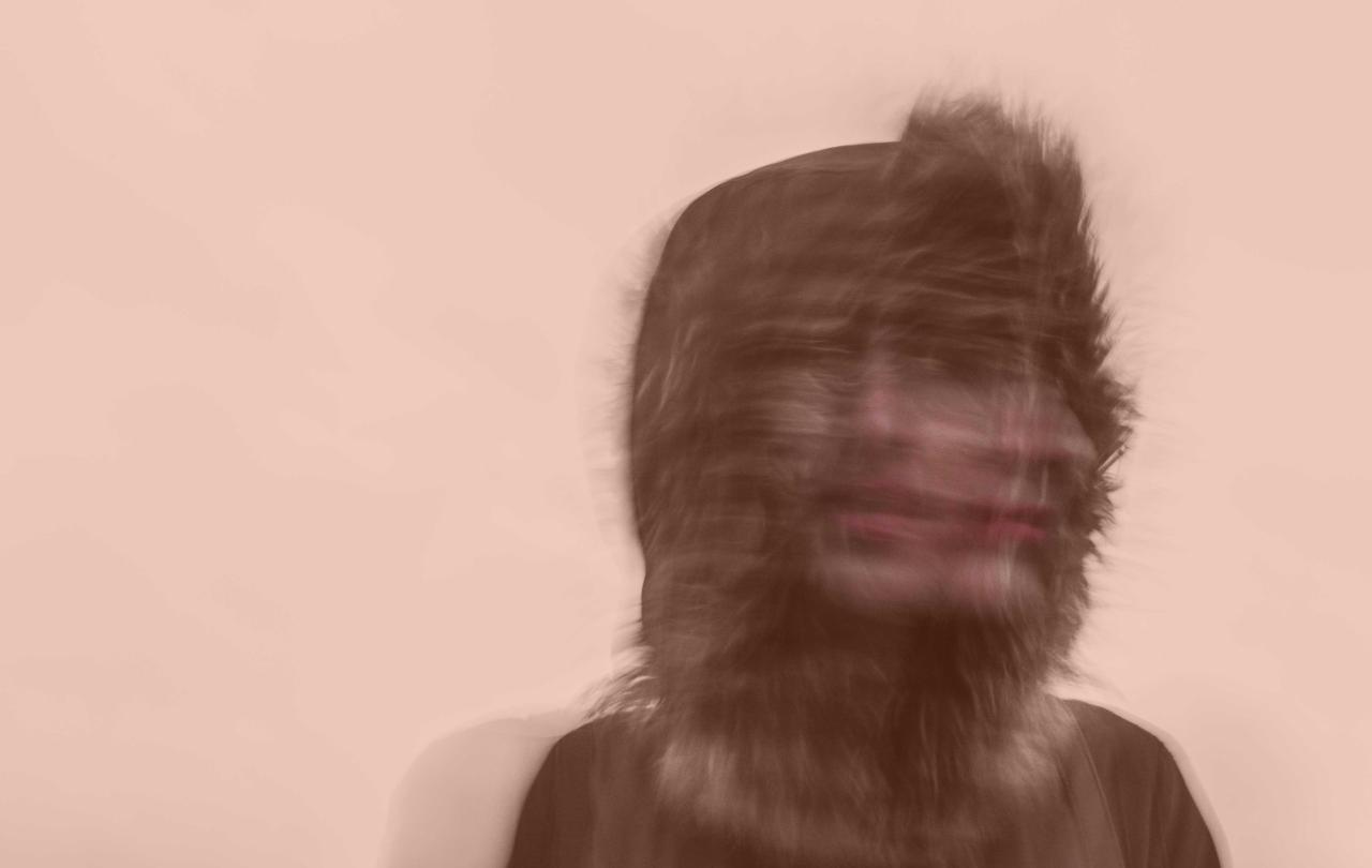 A blurred exposure of a person under a hood turning their head to the side.