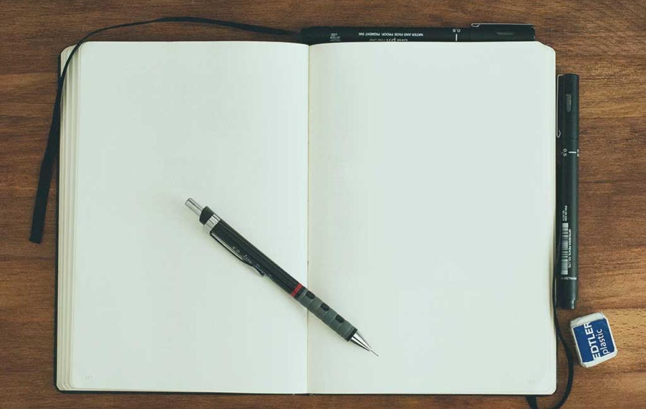 A notebook is open at two blank pages. a pen rests across the page.s.