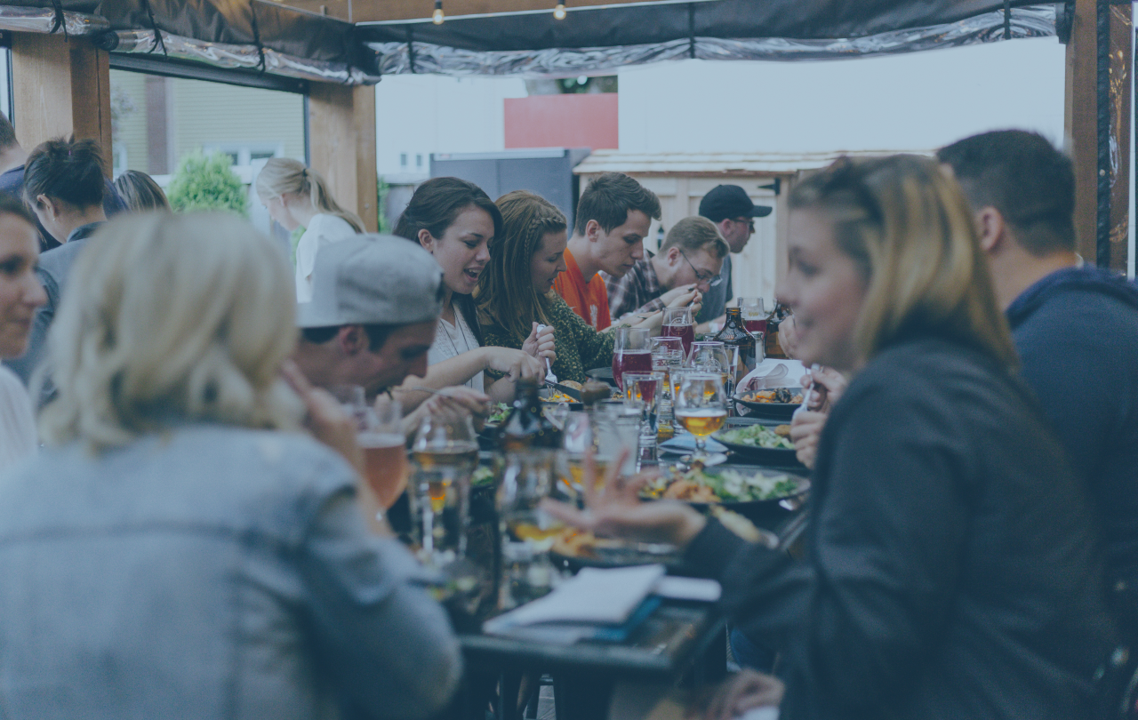 A large group of friends sit at a crowded table and share a meal together.