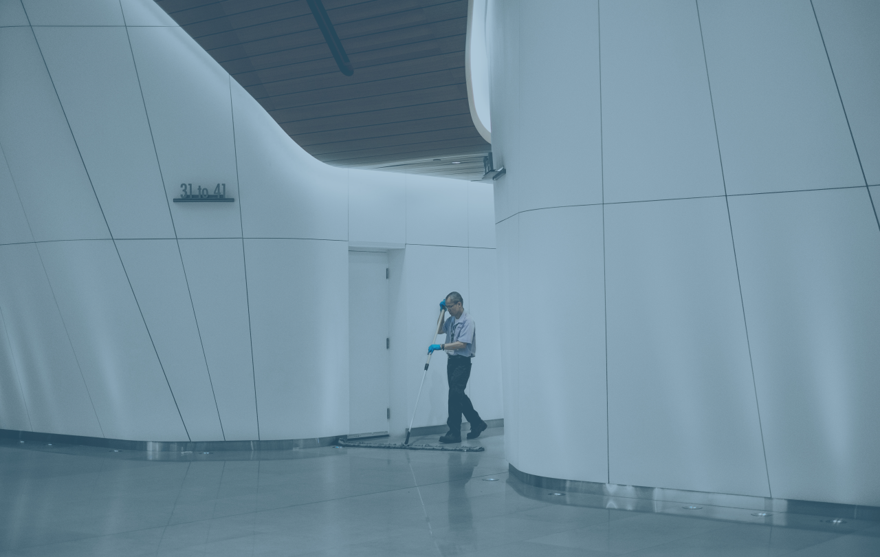 A cleaner sweeps between large white interior walls of a concourse.