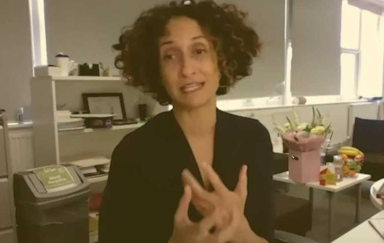 A head teacher sits at her desk, holding her hands in a gesture in front of her.