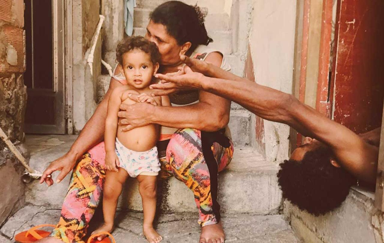 A mother sits with a toddler standing in front of her. The father appears from the side lying on his back reaching an arm out.