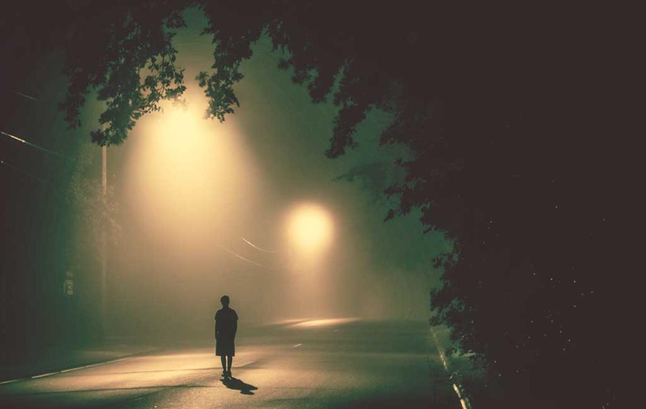 A person stands in a road under misty street lights.