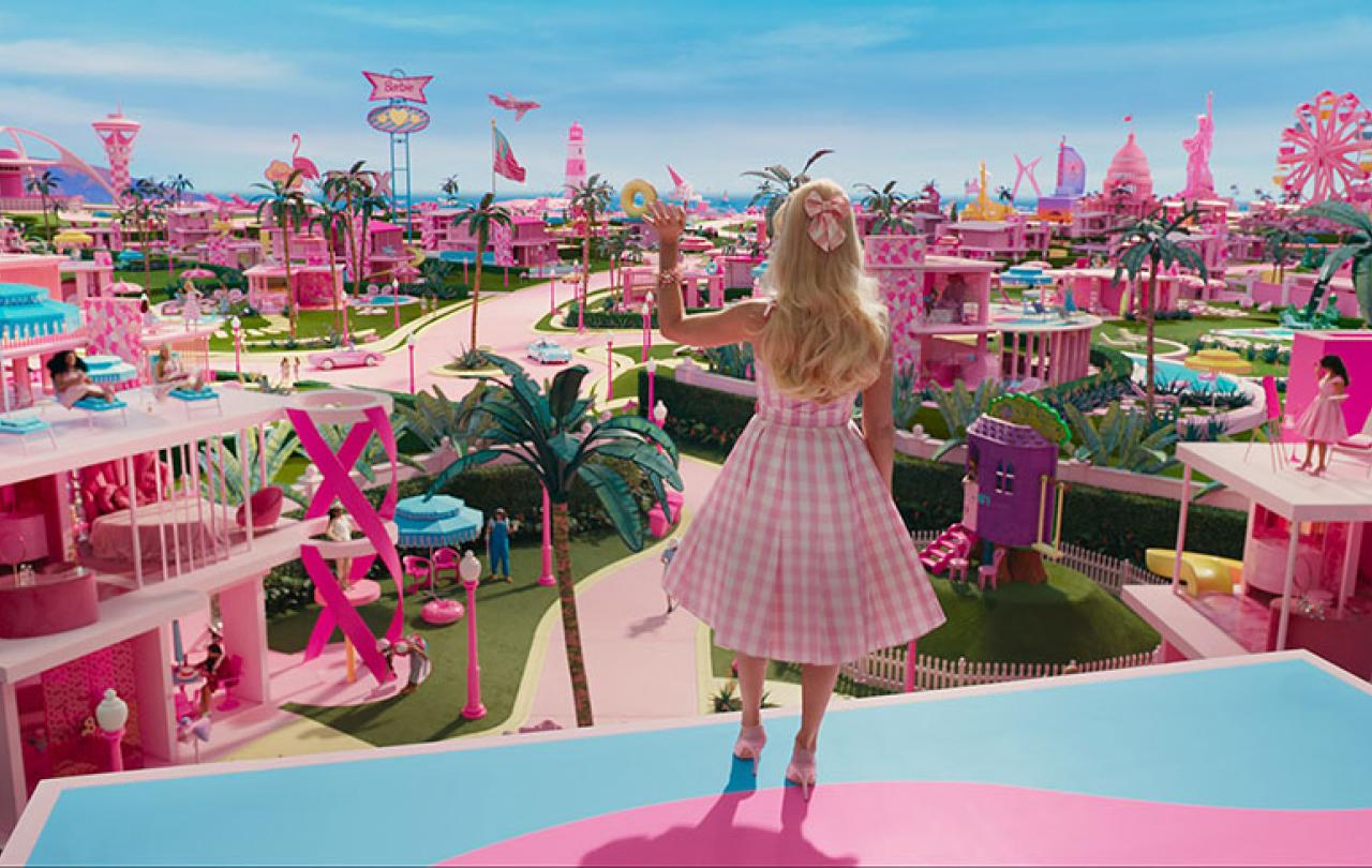 Barbie stands on a balcony and waves while looking out over her city.