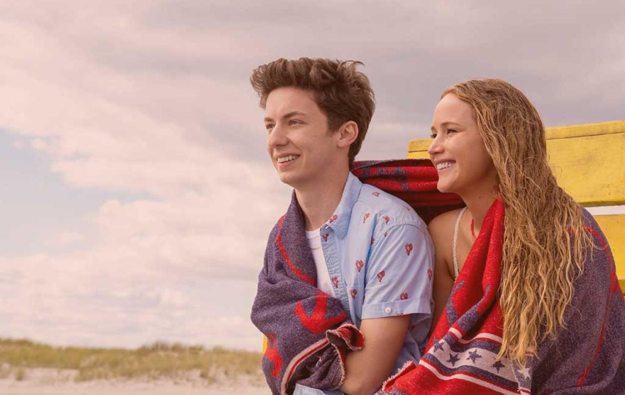 A young couple sit next to each other on a beach sharing a towel.