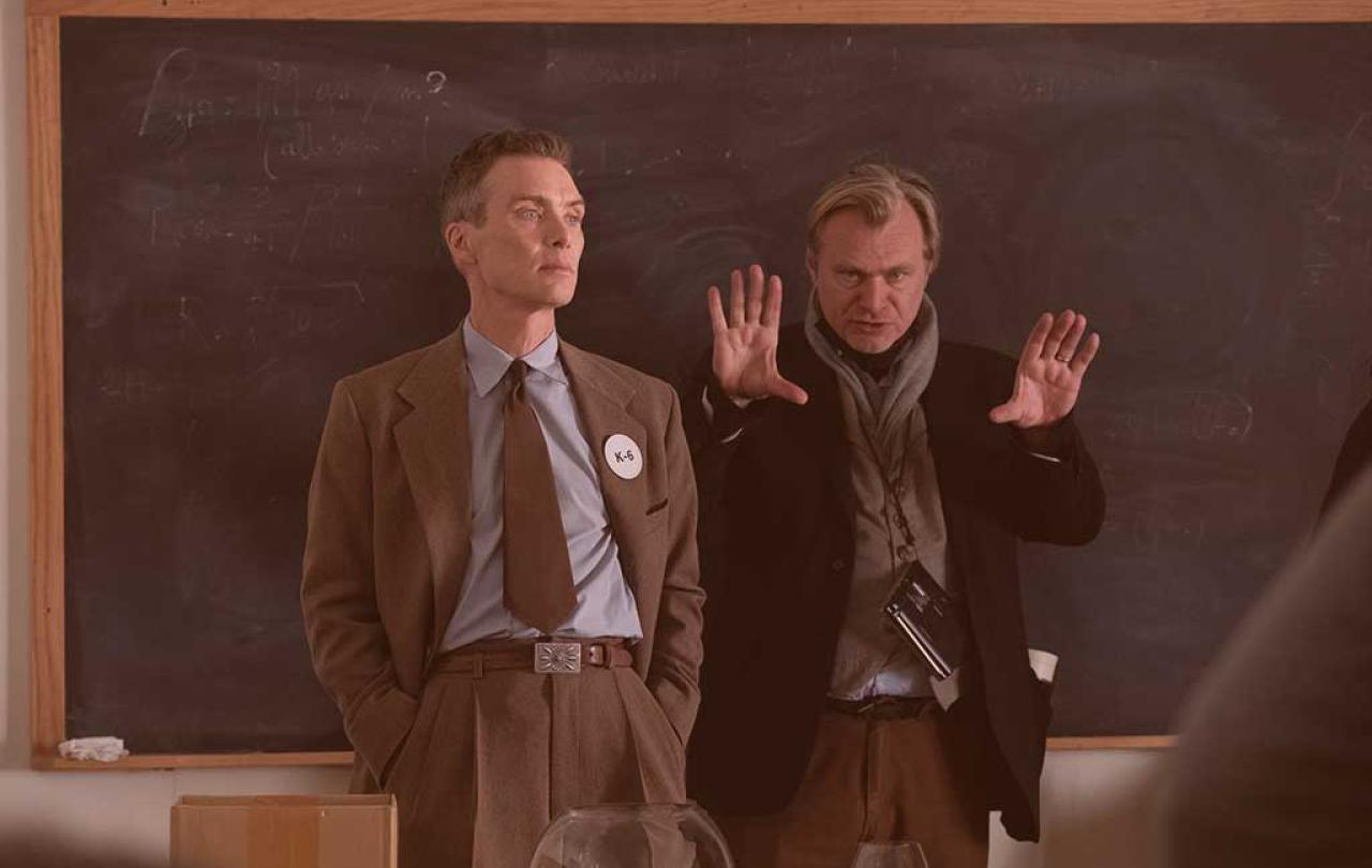 An actor looks on as a film director stands beside him staring with his hands raised.