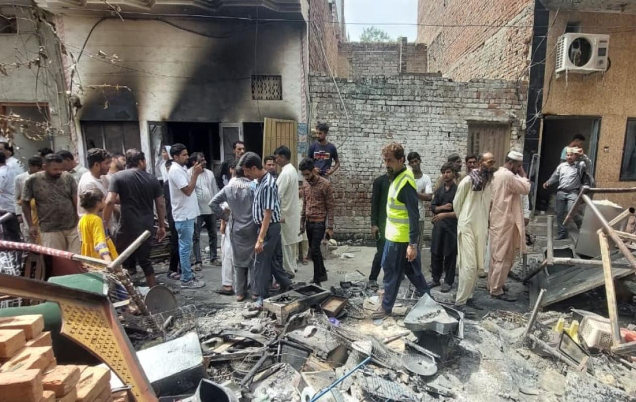 A crowd of people inspect fire damaged debris outside a burnt-out church.