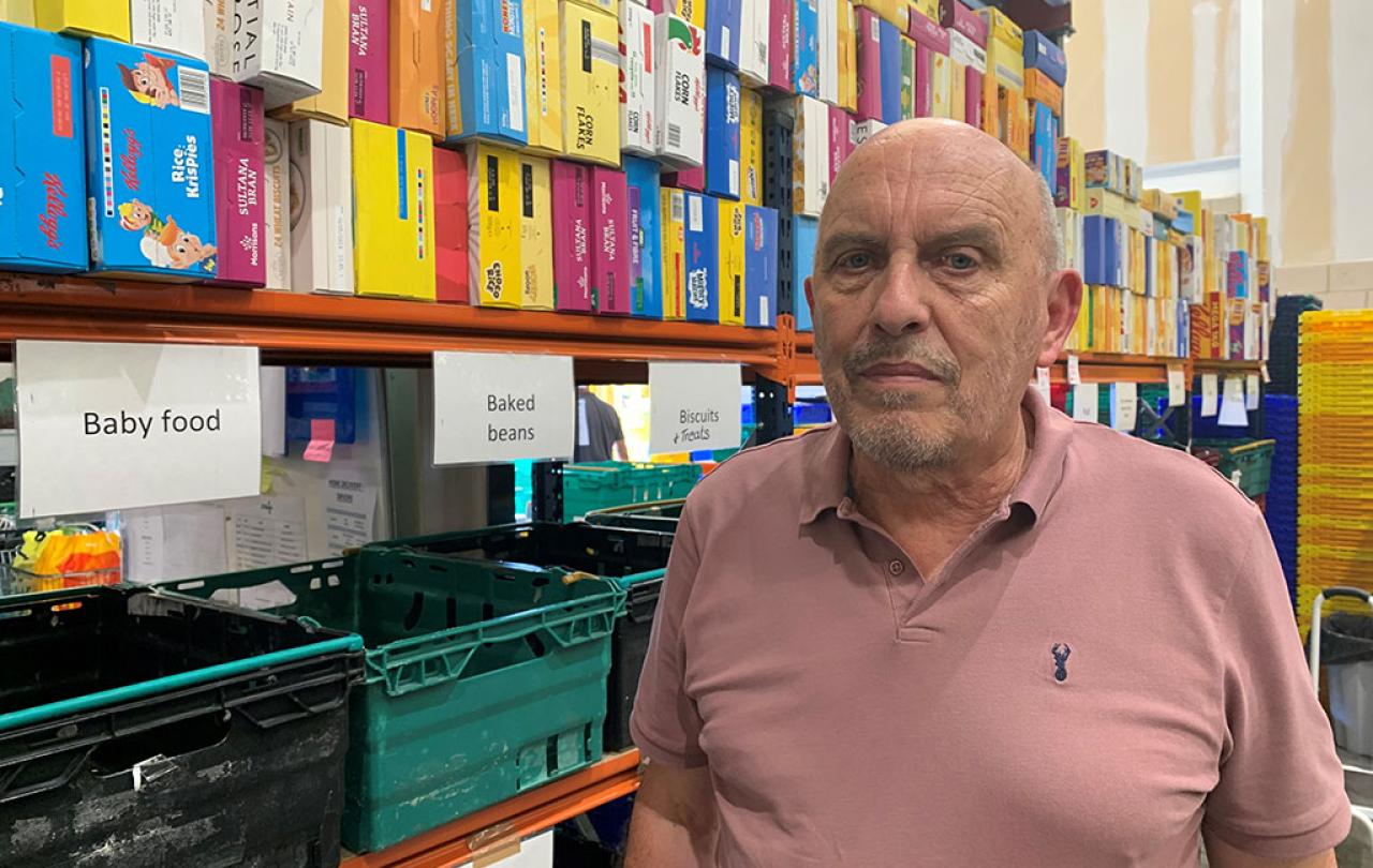 A man stands in front of a food bank's shelves of cereals and boxes labelled by foot type.