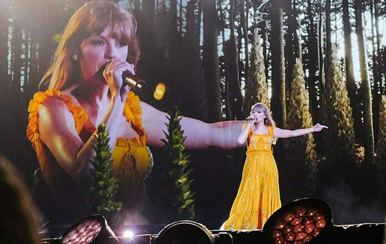 Taylor Swift wears a long yellow dress and signs with an outstretched arm against a backdrop of woods and a close up her singing beside it.