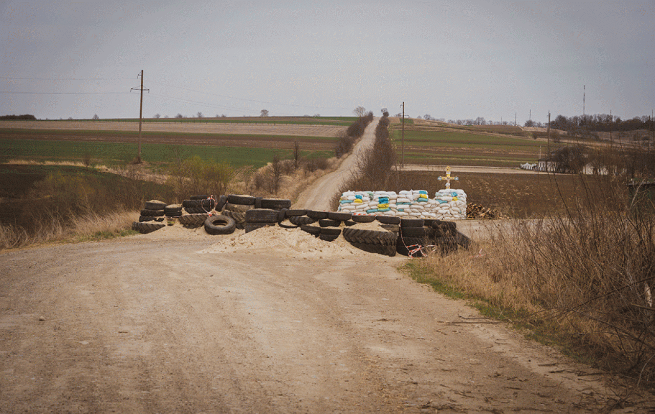 a dirt barricade blocks a cross roads, behind which stands a roadside cross