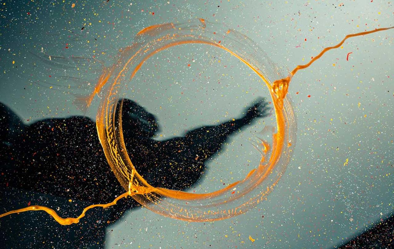 An abstract shadow of a human reaching an hand skyward is overlaid by a trace of orange line that becomes a circle