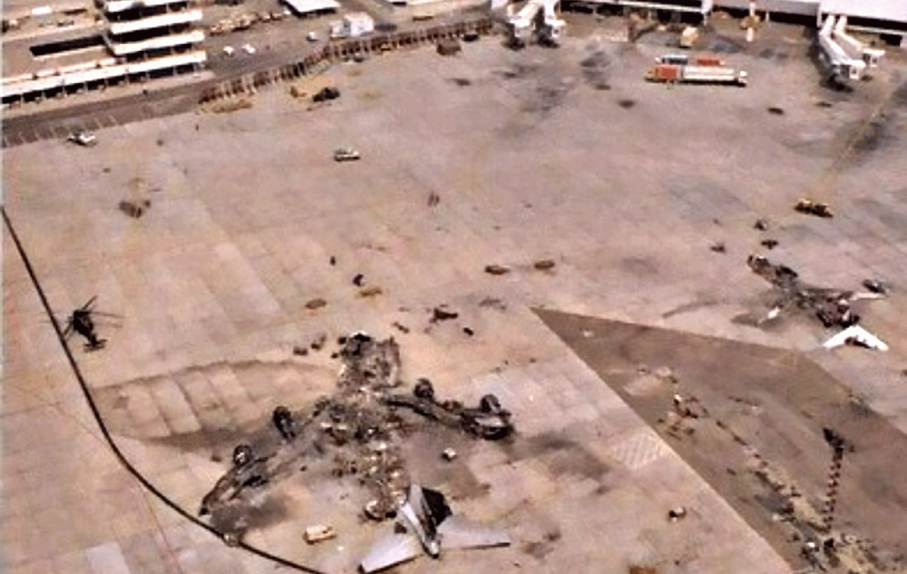 A destroyed airliner lies on the apron of a war-torn airport.