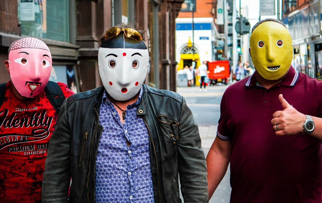 Three men wearing pink, spotty and yellow face masks stand in the street.