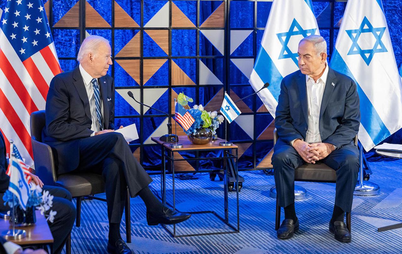 Two country leaders sit in chairs next to each other with their country's flags behind