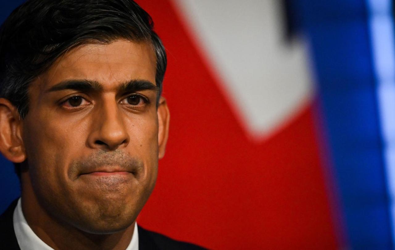 A cropped image of the face of RIshi Sunak with colours of a flag behind him