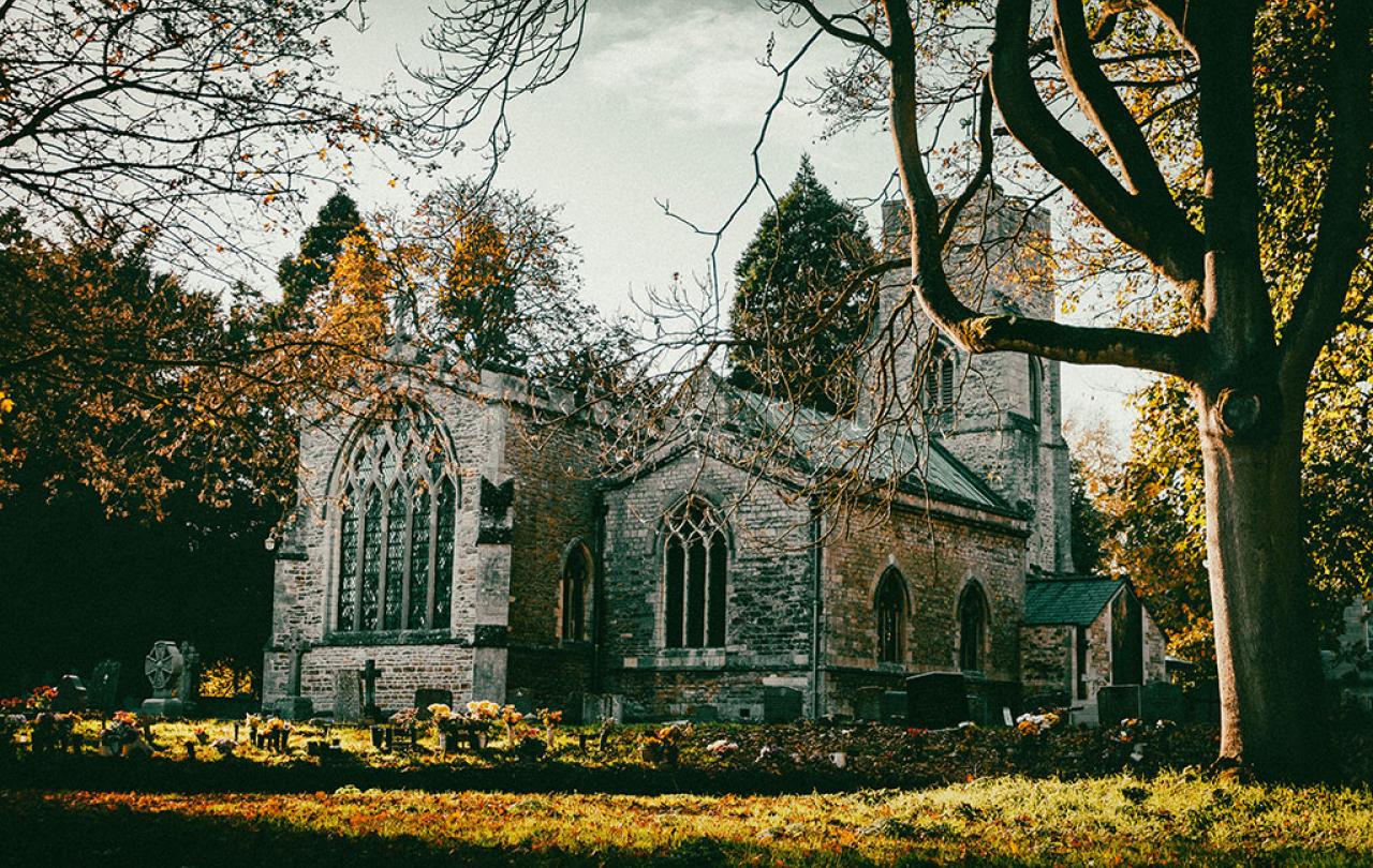 An autumnal scene of a church yard and church framed by leafless trees.