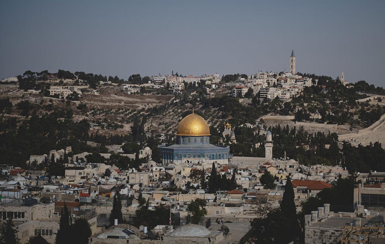 A blue and gold domed mosque sits surrounded by old stone buildings of a city.