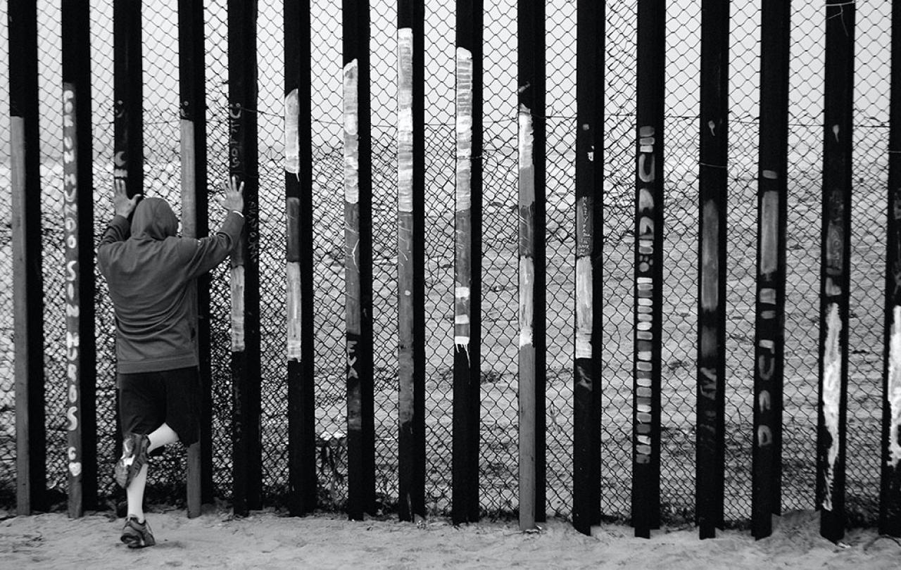 A person holds the vertical tall steel bars of a border fence.