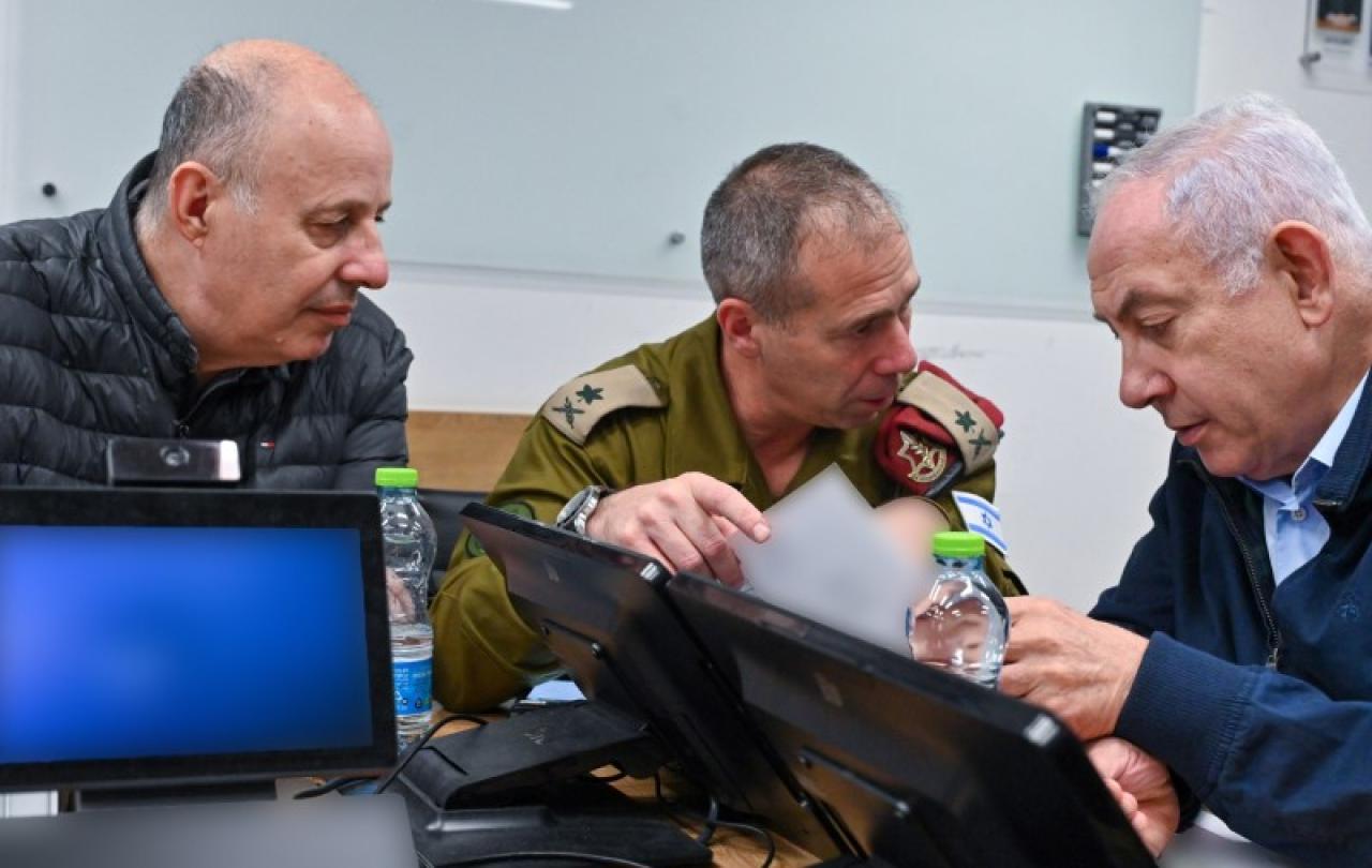 Three men huddle around a laptop and talk animatedly.