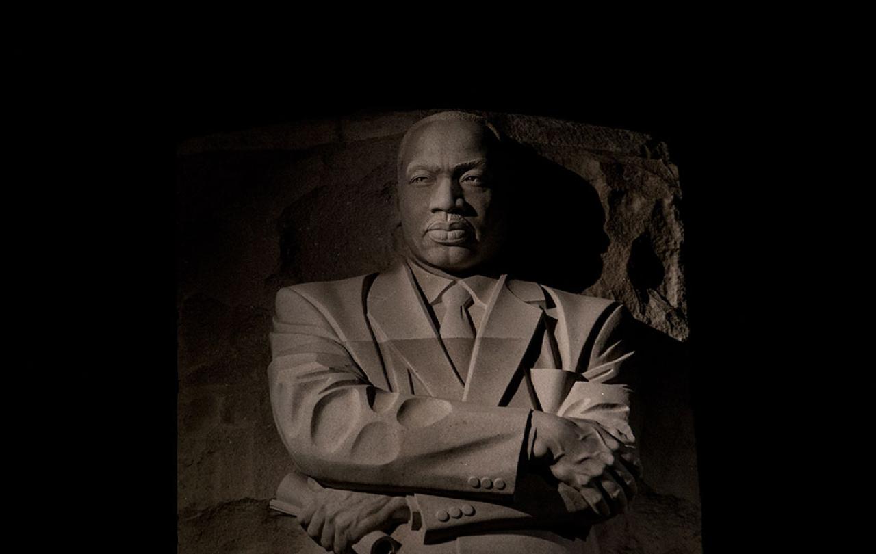 An imposing stone statue of Martin Luther King standing with his arms crossed.