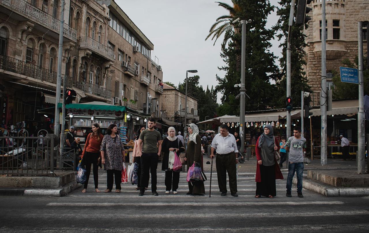 A line of people, some old, some young, wait to cross a road.