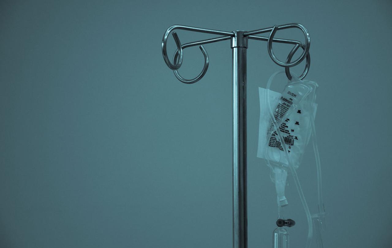A IV drip bag hangs from a medical stand.