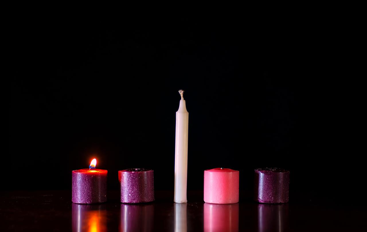 Five candles sit in a row against a dark background, only one is lit.