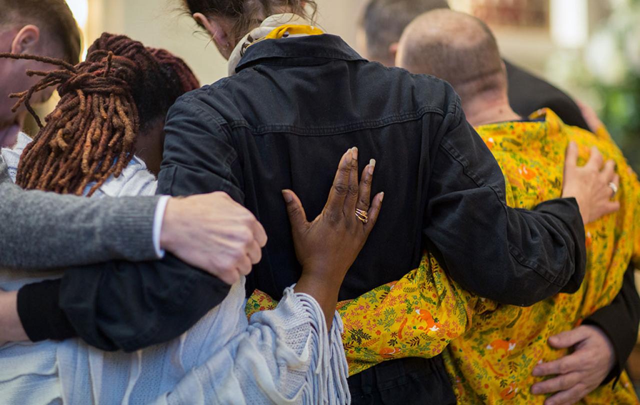 A group of grieving friends with their hands on each others backs.