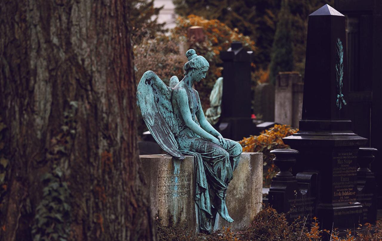 A bronze statue of a resting angel sits atop a low stone grave.