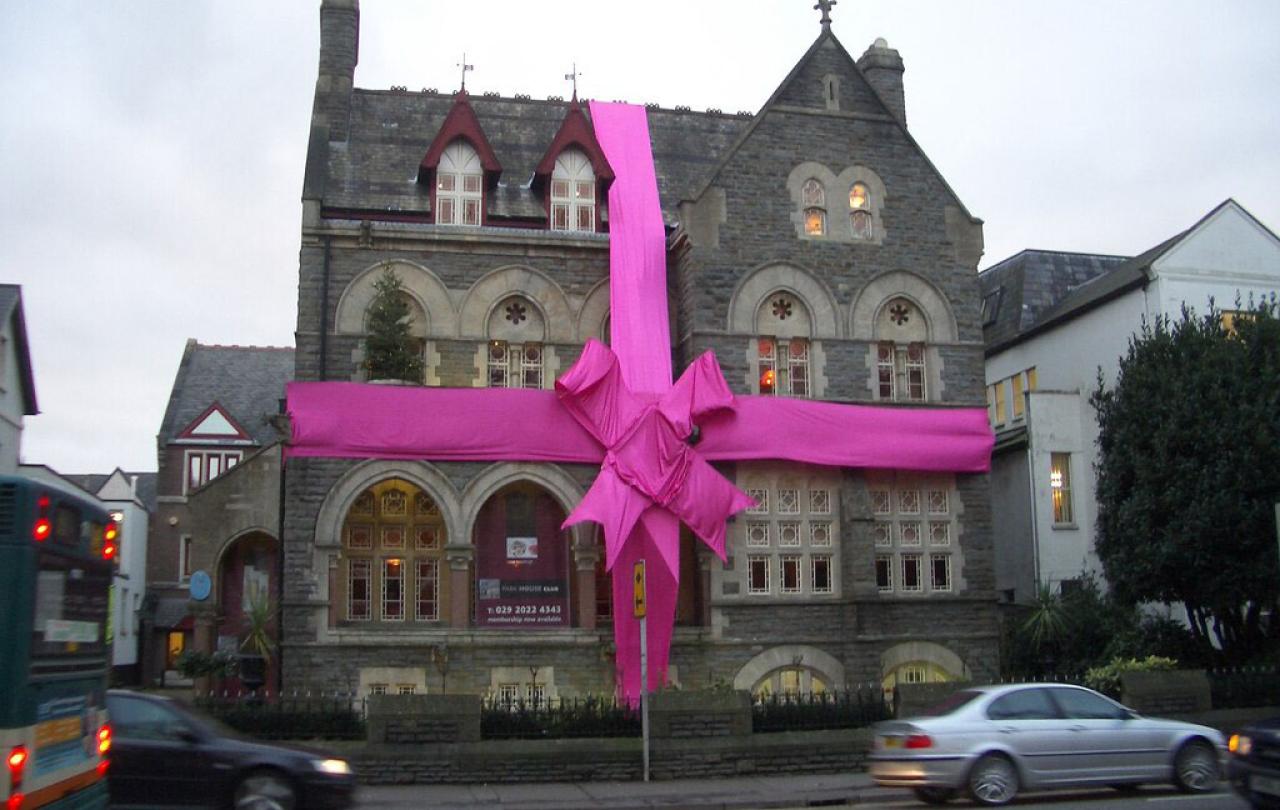 A large stone house is wrapped in a red ribbon and bow.