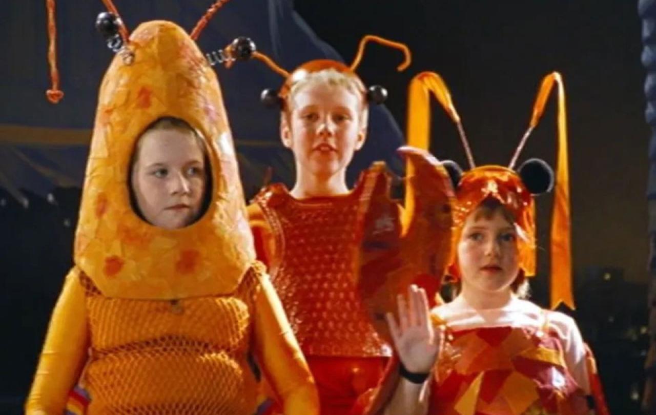 Three children dressed as orange lobsters stand sheepishly on a stage.