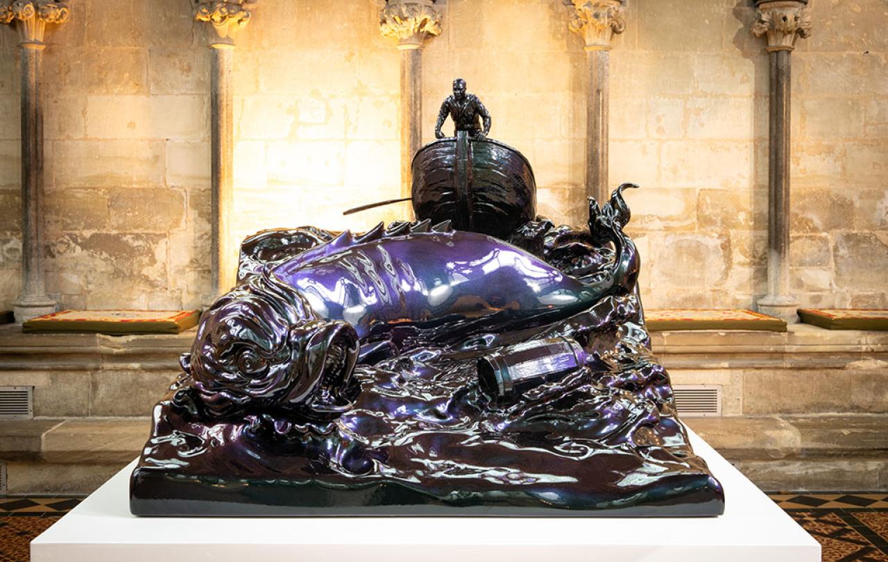 A bronze sculpture of a small boat and sea monster tossed in the waves.